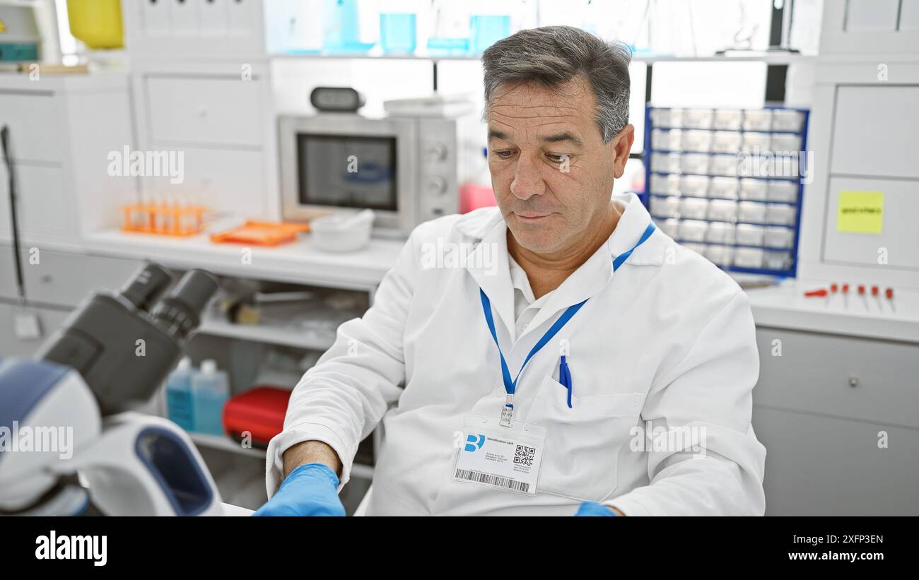 A mature man in a laboratory wearing a lab coat and gloves examining a ...