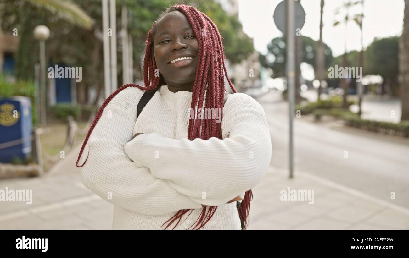 A joyful african woman with red braids posing on an urban street exudes ...