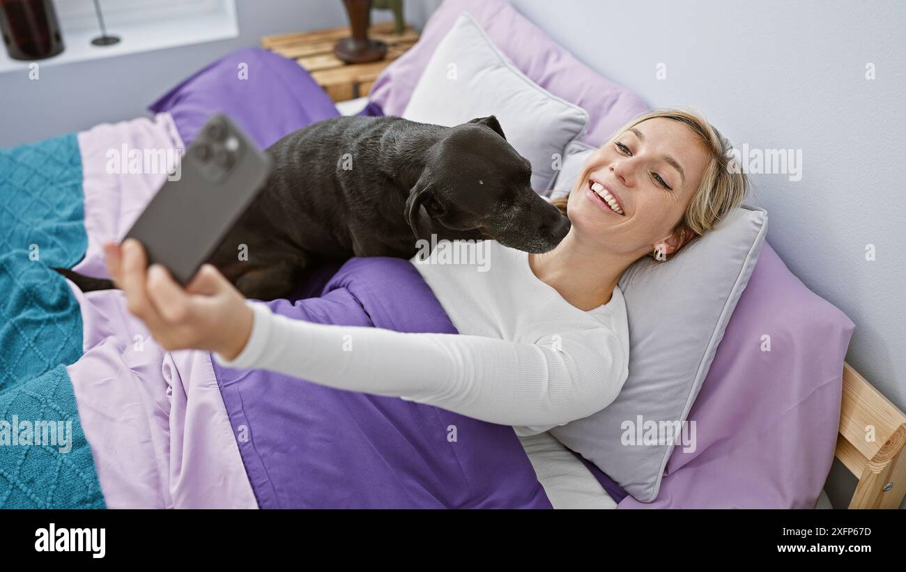 A smiling young woman takes a selfie with her black labrador in a cozy ...