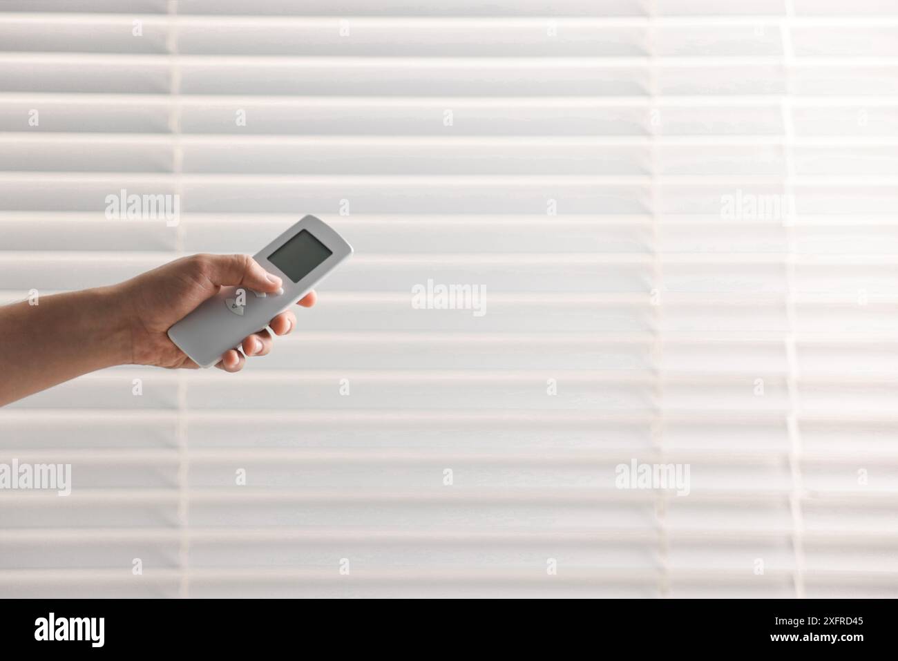 Man using remote control to adjust window blinds indoors, closeup. Space for text Stock Photo