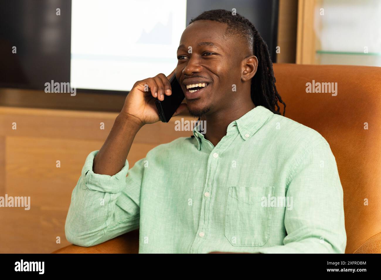 Smiling man talking on smartphone while sitting in office chair Stock Photo