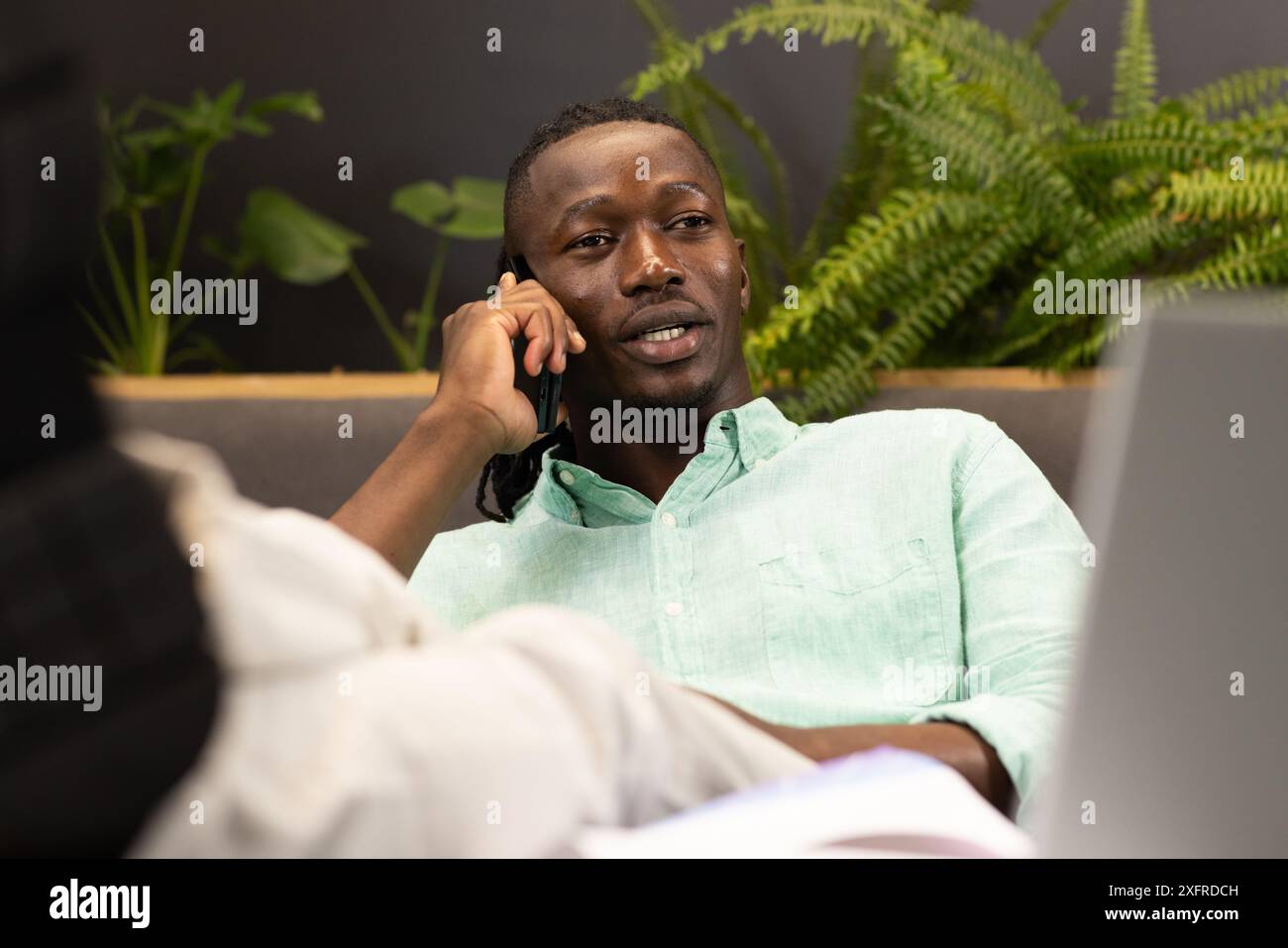 Talking on smartphone, man working on laptop in modern office setting Stock Photo