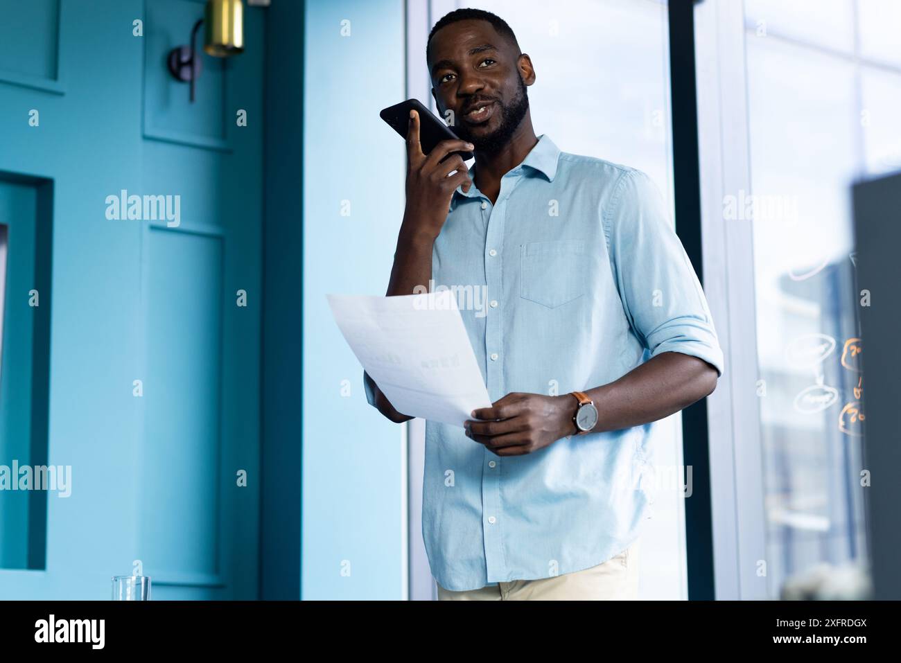 Holding document, man speaking on smartphone in modern office setting Stock Photo