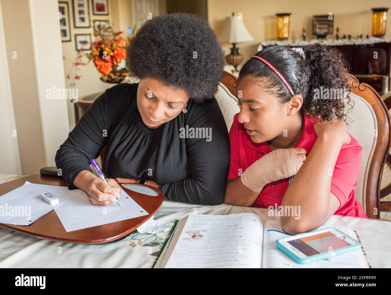 African American mother helping daughter with homework at dining table ...