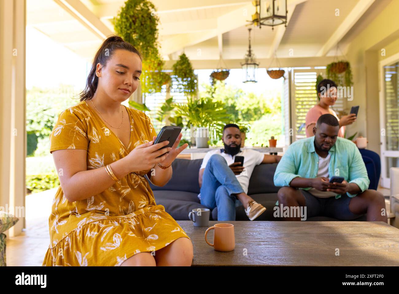 Using smartphones, group of diverse friends relaxing together on patio Stock Photo
