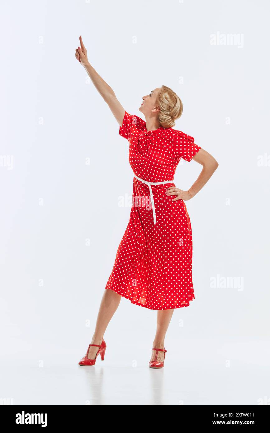 Elegant woman in red polka dot dress and matching heels points upwards with  enthusiasm, isolated on white background Stock Photo - Alamy