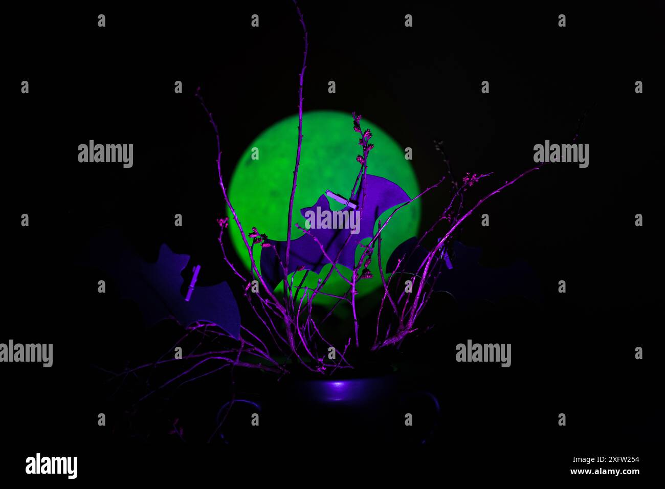 Cutout bats silhouette attached to branches in purple neon light against a green moon. Spooky arts and craft for kids Stock Photo