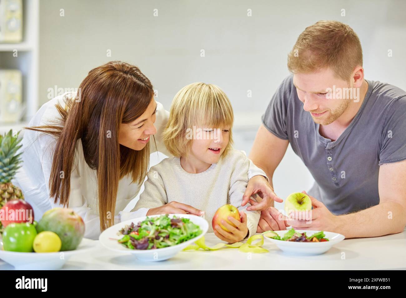 Family in the kitchen. Parents and son. Healthy eating. Healthy growth. Eating an apple. Stock Photo