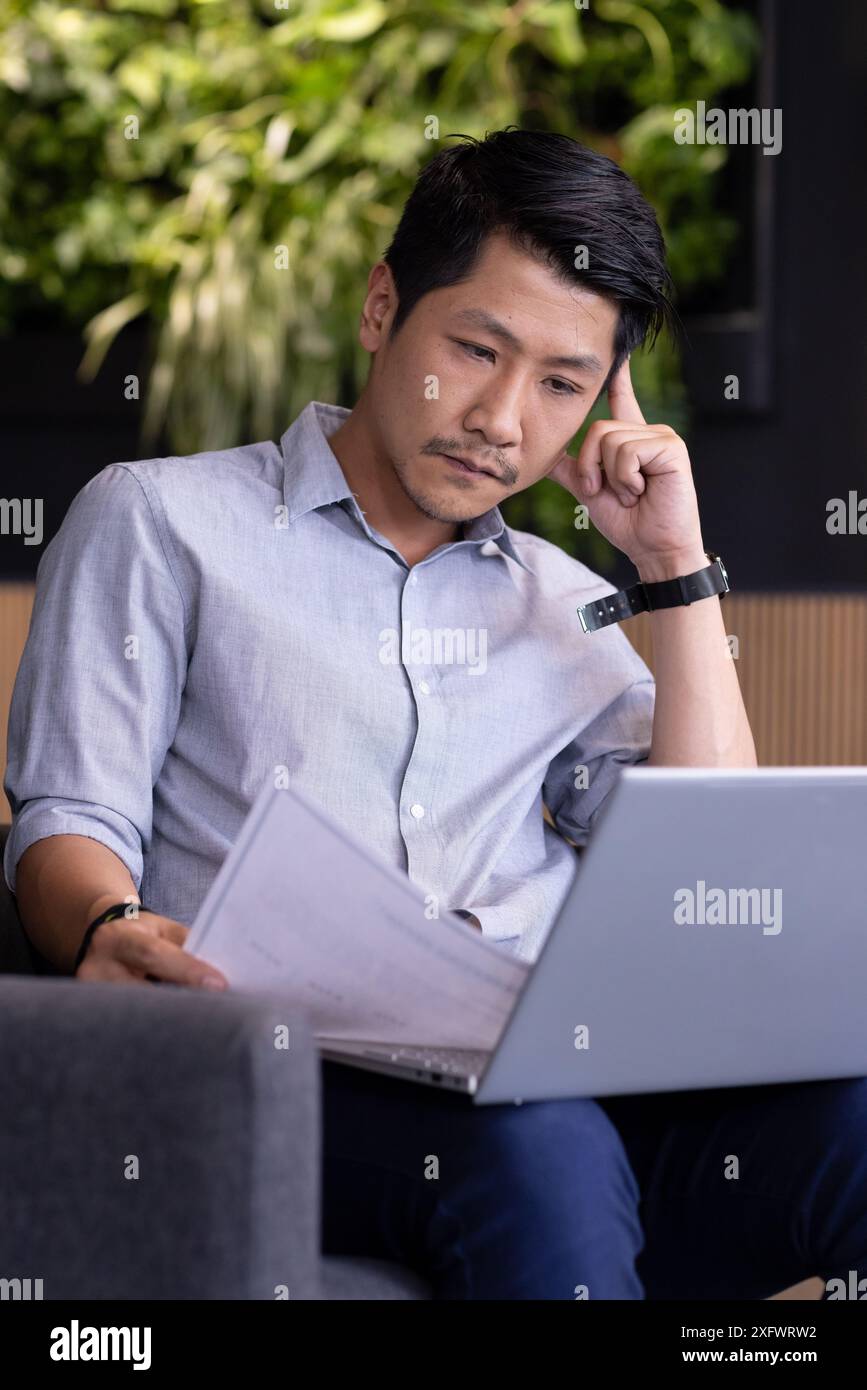 Working from office, man reviewing documents while using laptop on couch Stock Photo