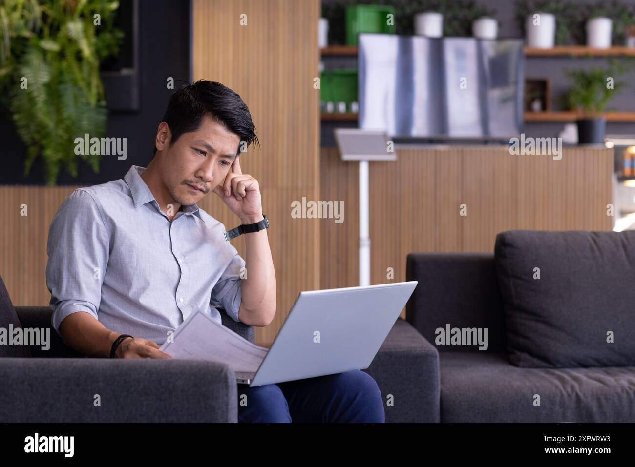 Working from office, man using laptop and reviewing documents on couch, copy space Stock Photo
