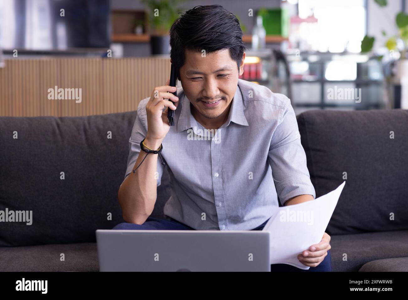 Talking on phone, man holding documents and using laptop while working from home Stock Photo