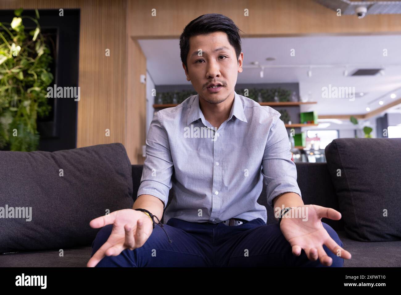 Man sitting on couch, gesturing while having conversation in modern office Stock Photo