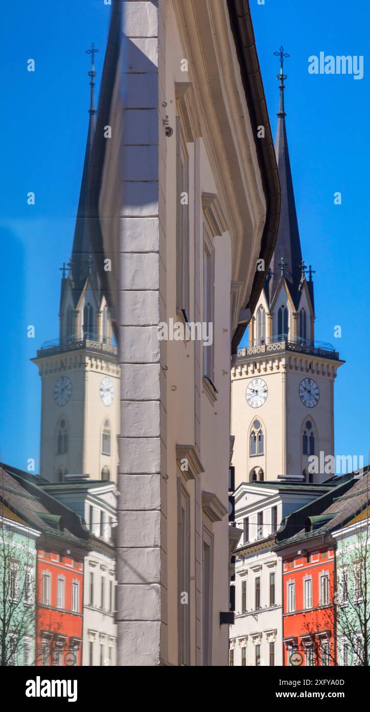 symmetry of colorful buildings and parish church bell tower reflected in a shop window of the old town of villach, carinthia, austria Stock Photo