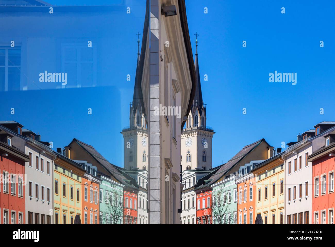 symmetry of colorful buildings and parish church bell tower reflected in a shop window of the old town of villach, carinthia, austria Stock Photo