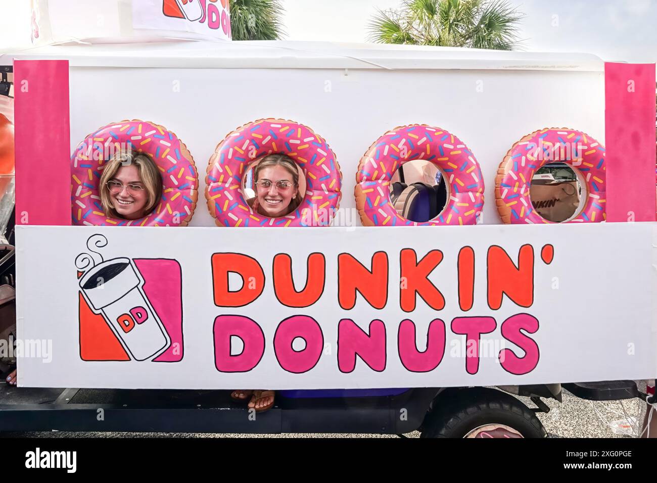 Sullivans Island, United States of America. 04 July, 2024. Young women look out from donut shaped portals in a golf cart decorated like a Dunkin' Donut box during the annual Bicycle and Golf cart parade celebrating Independence Day July 4, 2024 in Sullivans Island, South Carolina. Credit: Richard Ellis/Richard Ellis/Alamy Live News Stock Photo