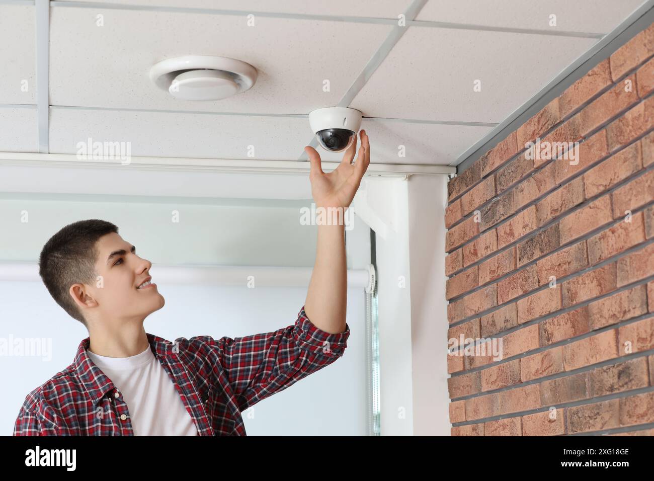 Technician installing CCTV camera on ceiling indoors Stock Photo