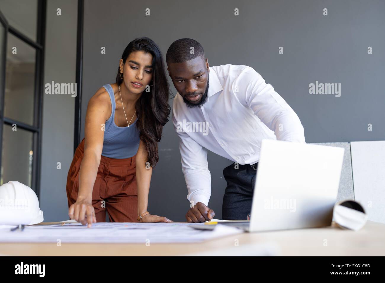 Collaborating on project, colleagues reviewing blueprints and using laptop in office Stock Photo
