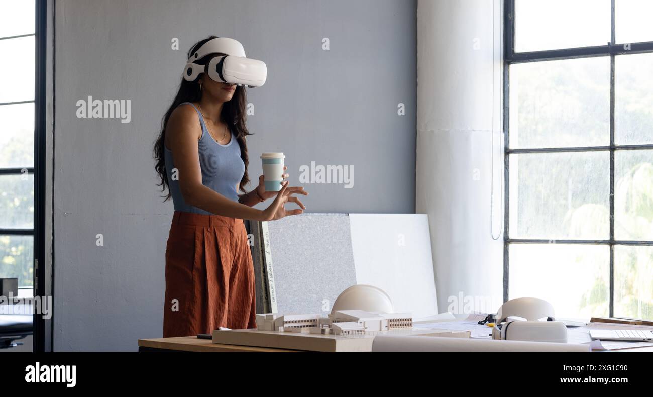 Using VR headset, woman holding coffee cup and working on architectural model, copy space Stock Photo