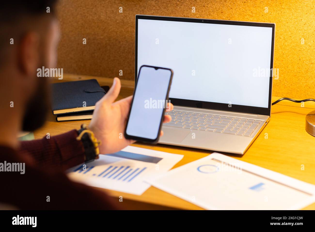 Using smartphone and laptop, man working from home with documents on desk, copy space Stock Photo