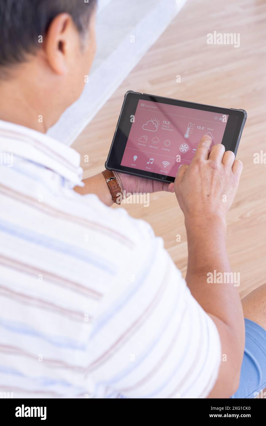 Using tablet, senior man controlling smart home devices with touchscreen interface Stock Photo