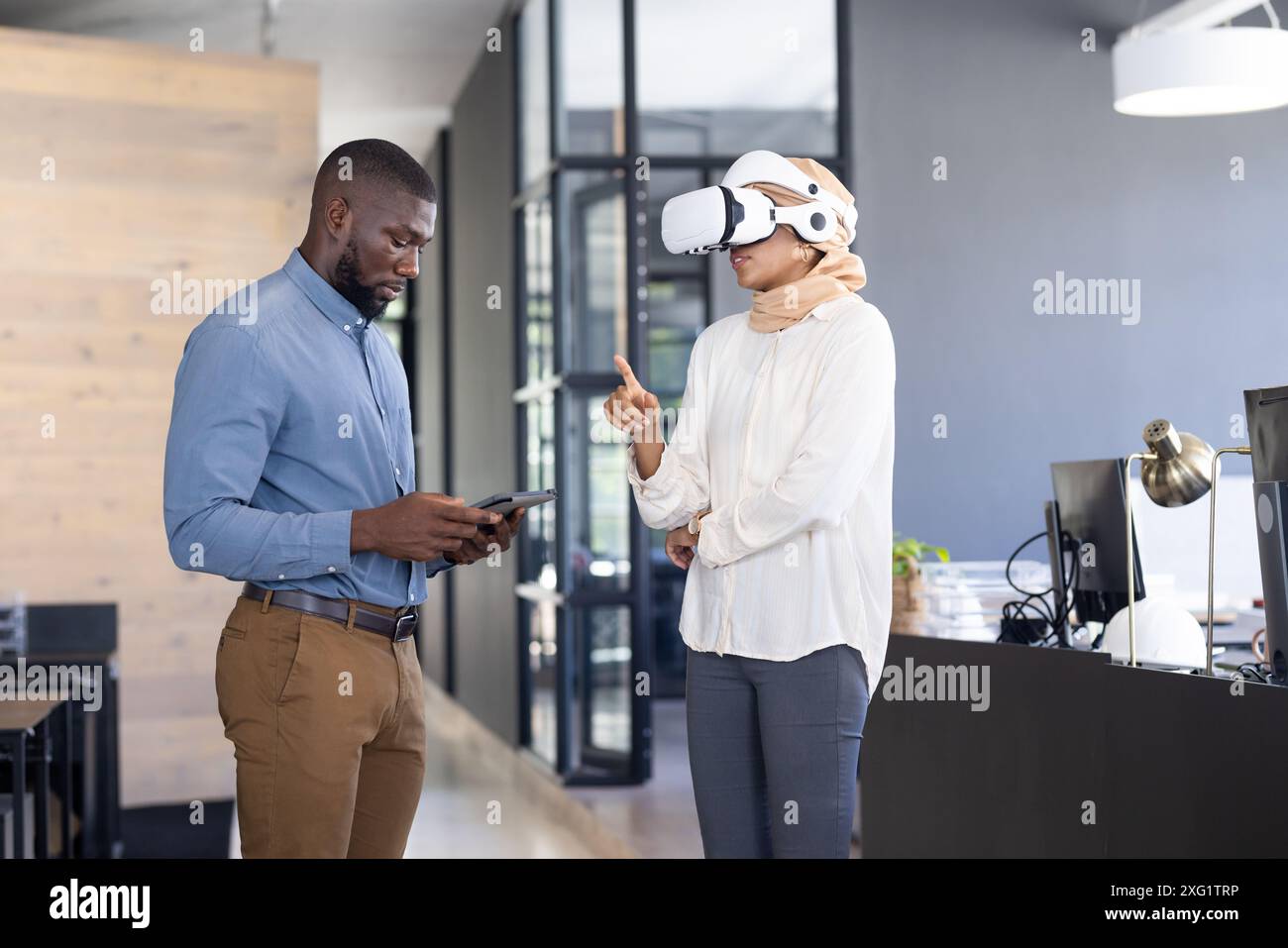Using VR headset, woman gesturing while man holding tablet in modern office Stock Photo