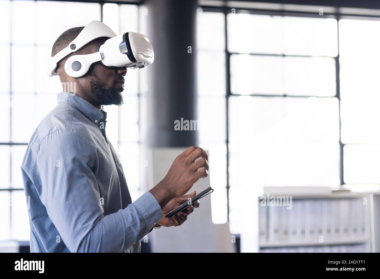 Using VR headset, man interacting with virtual environment while holding tablet Stock Photo