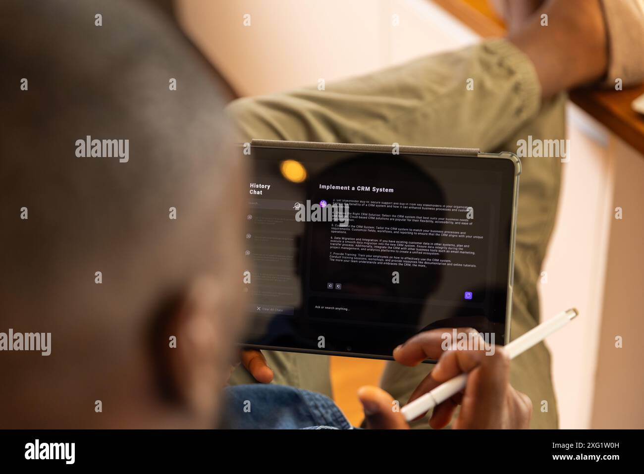 Using AI chatbot on tablet and stylus, man reading about implementing CRM system at home Stock Photo