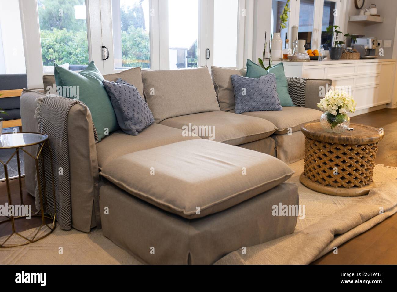 Decorative pillows on beige sectional sofa, round wicker table in cozy living room Stock Photo
