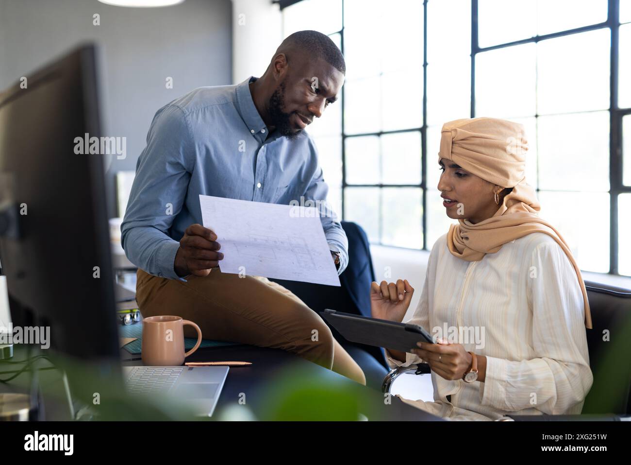 Discussing project, colleagues reviewing blueprint and using tablet in modern office Stock Photo