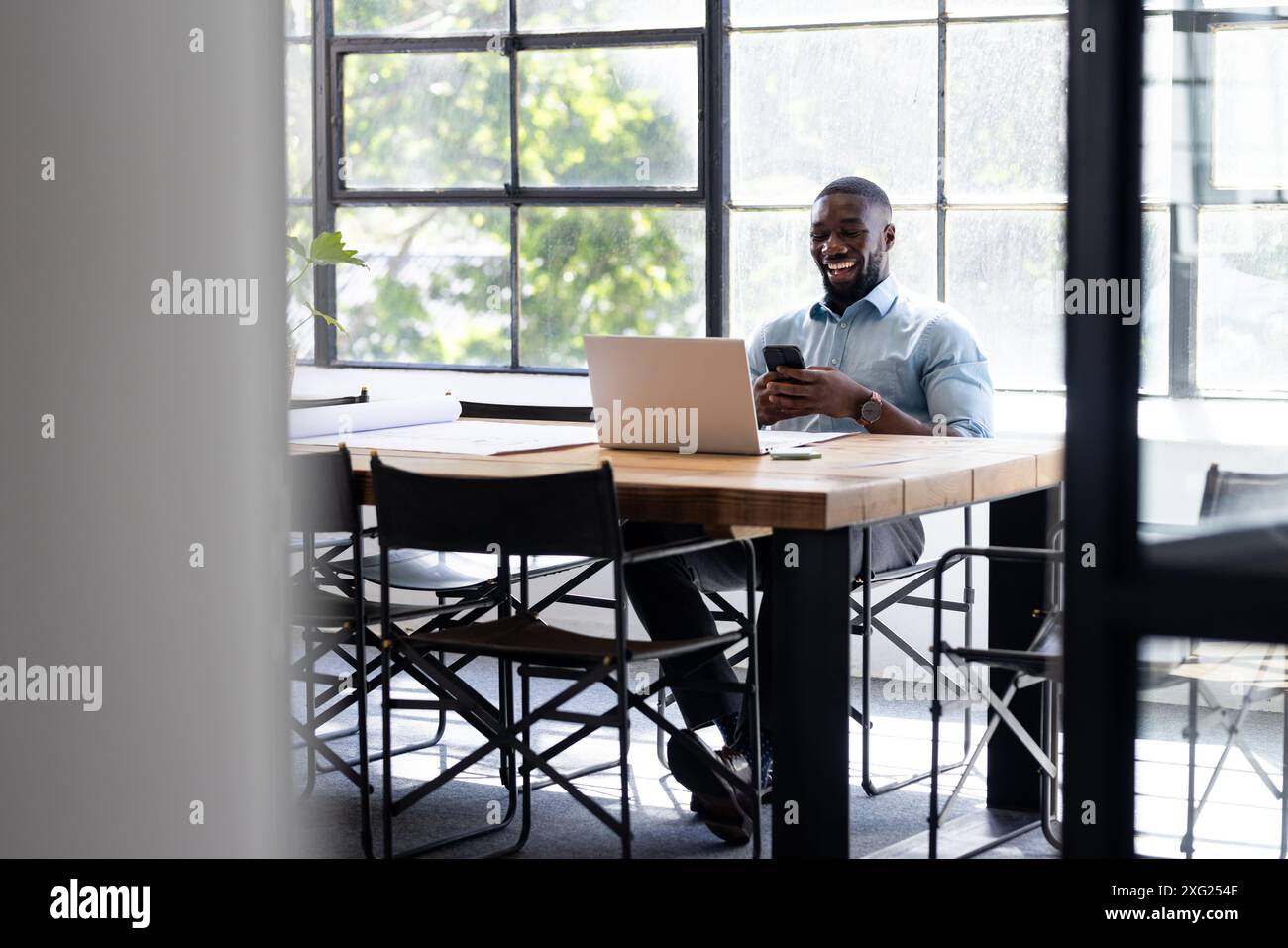 Using smartphone and laptop, man working and laughing in modern office setting Stock Photo