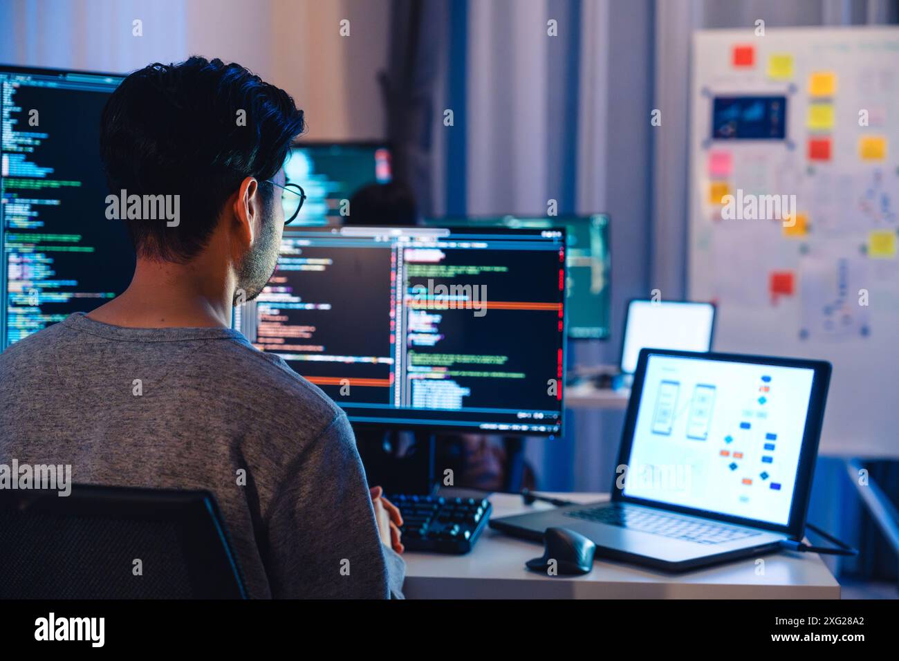 Asian software developers working on multiple screens displaying code and application diagrams at night in modern office Stock Photo