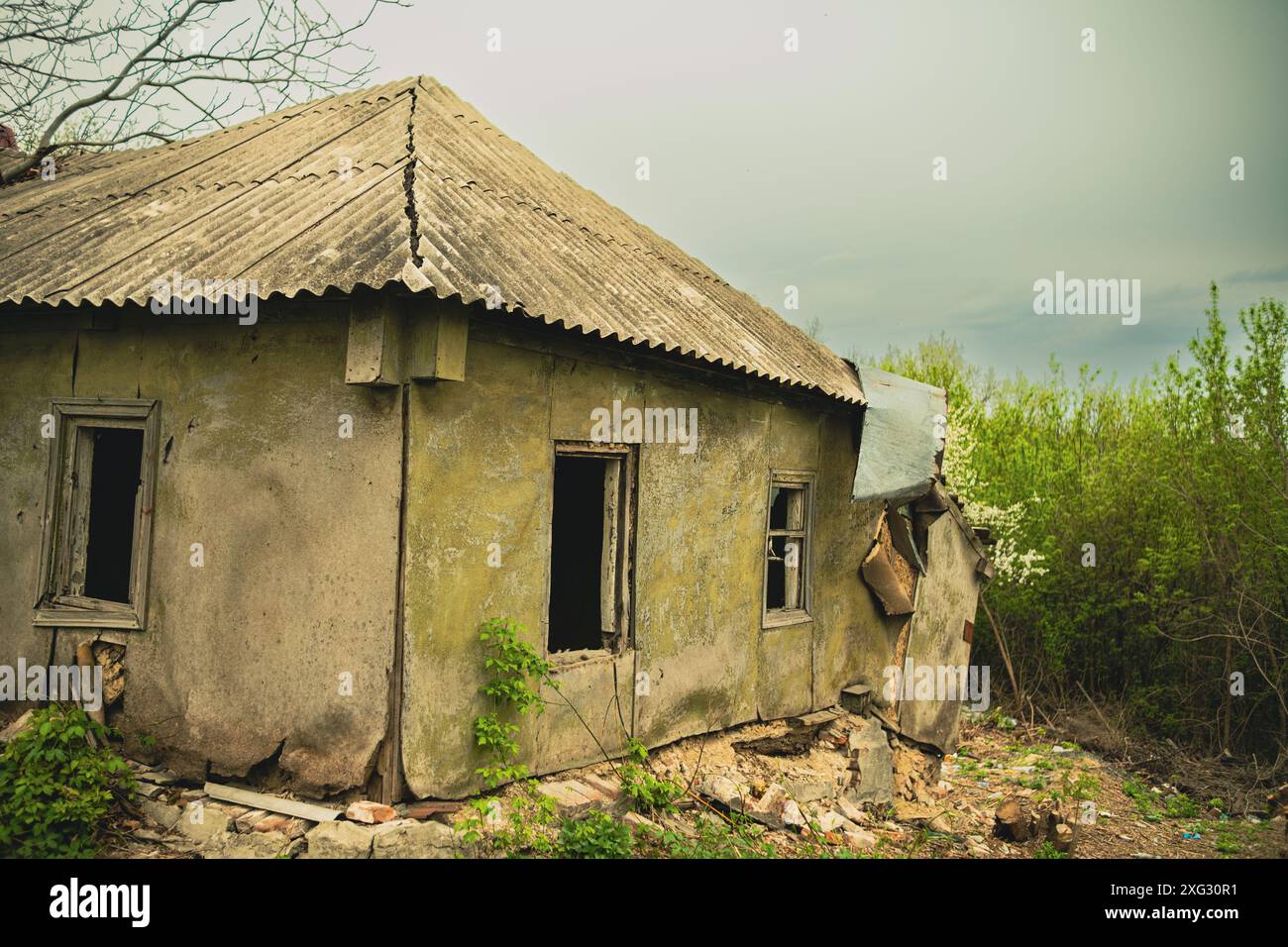 Dilapidated Rural Cottage on a Cloudy Day With Overgrown Vegetation. Abandoned house falling apart with nature taking over on an overcast day Stock Photo