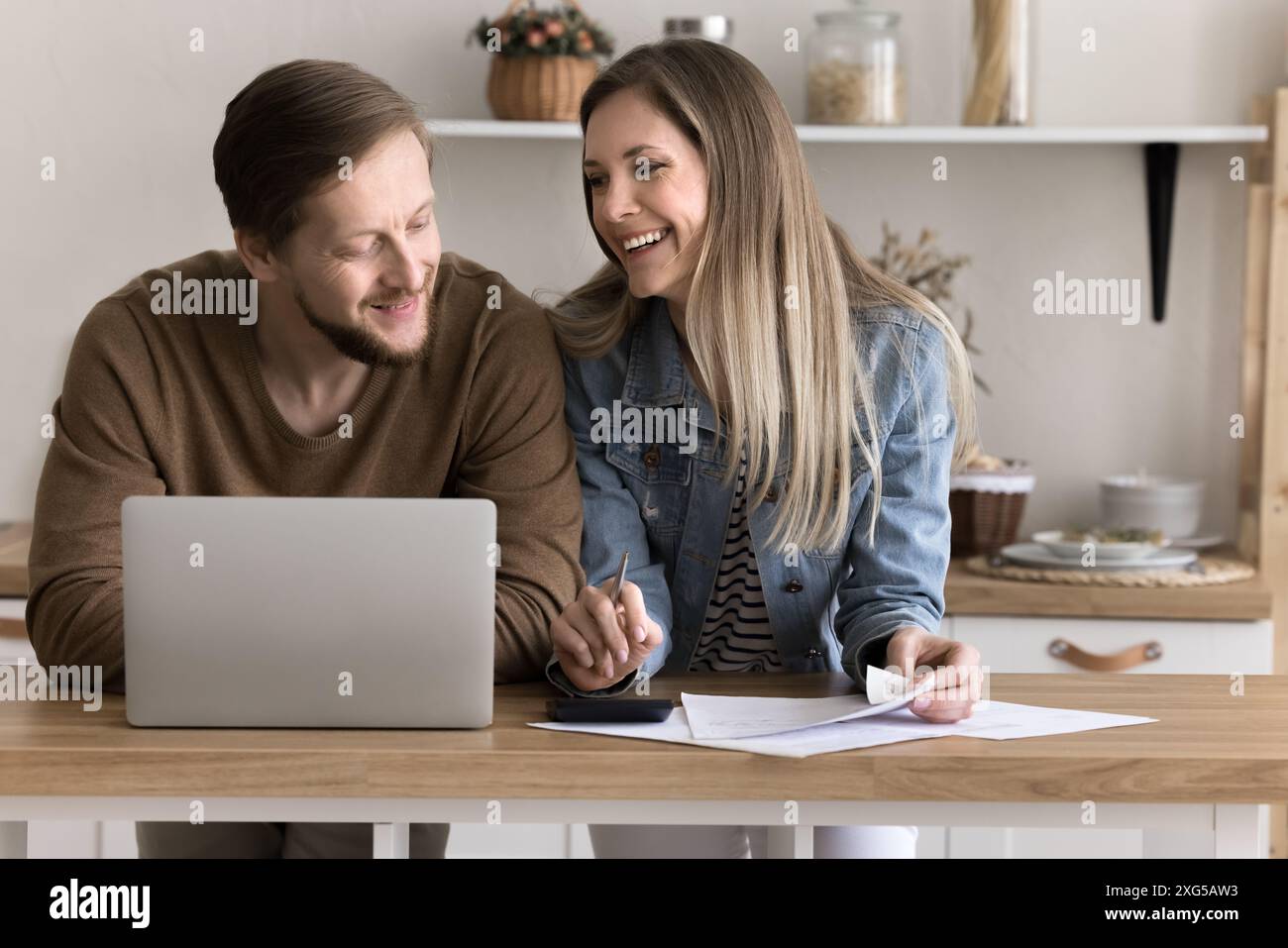 Smiling spouses do paperwork in home kitchen use laptop Stock Photo