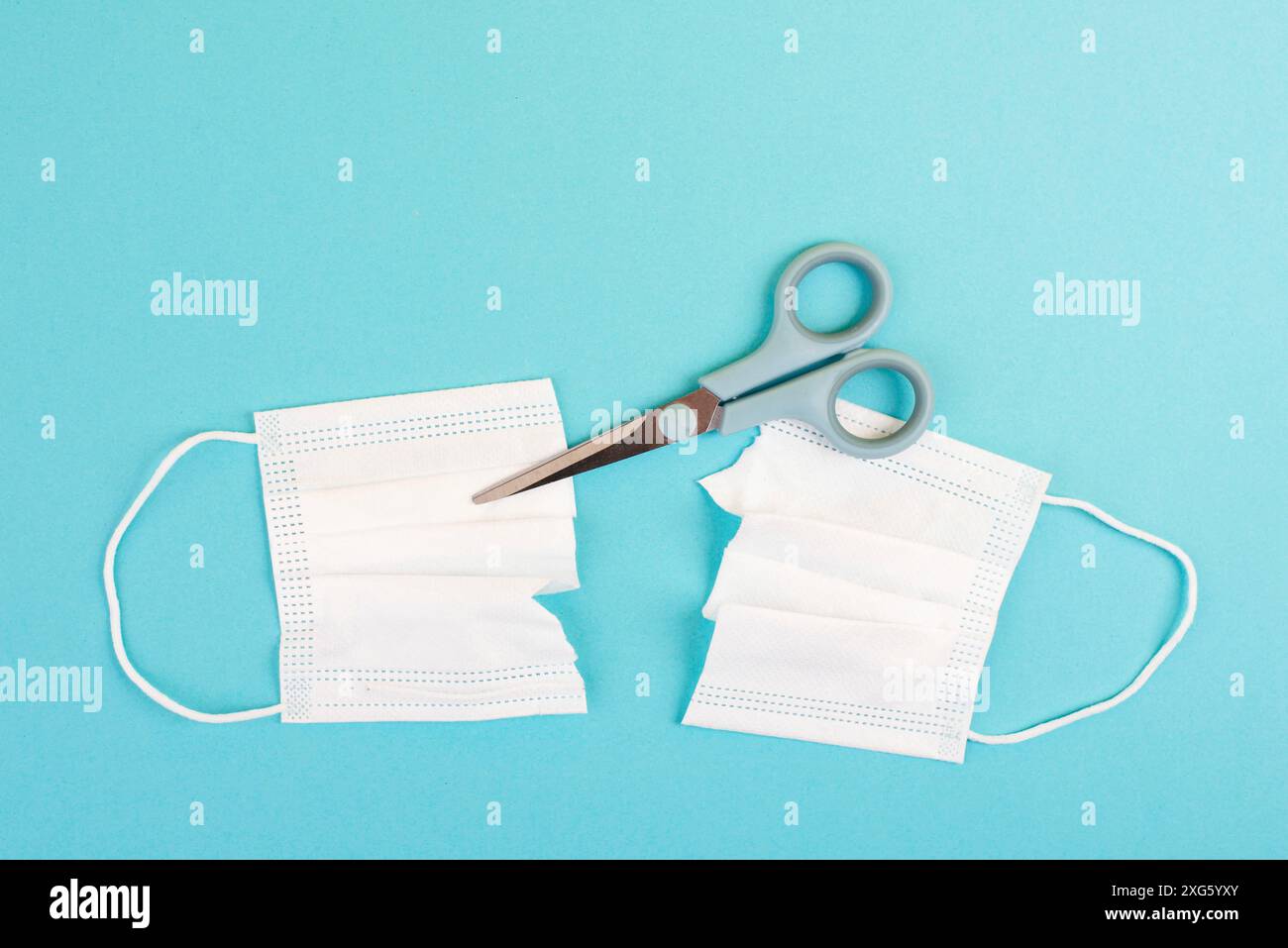 Covid-19 mask cut into two pieces with a scissor, end of pandemic, back to normal, epidemic Stock Photo