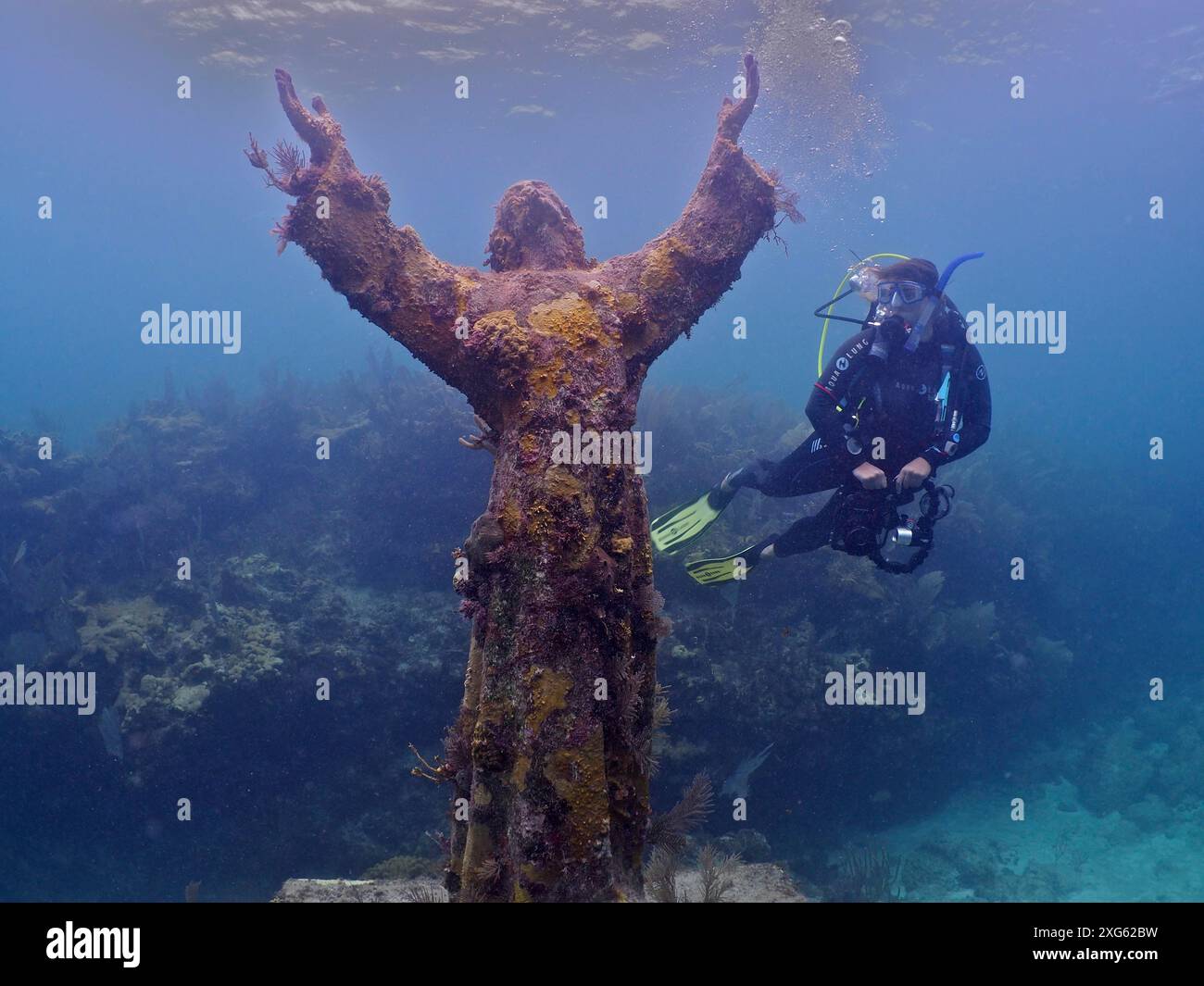 Diver with camera looking at an underwater statue of Jesus Christ