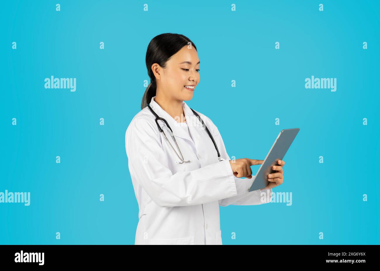 Woman Doctor in White Coat Using Digital Tablet Against Blue Stock Photo