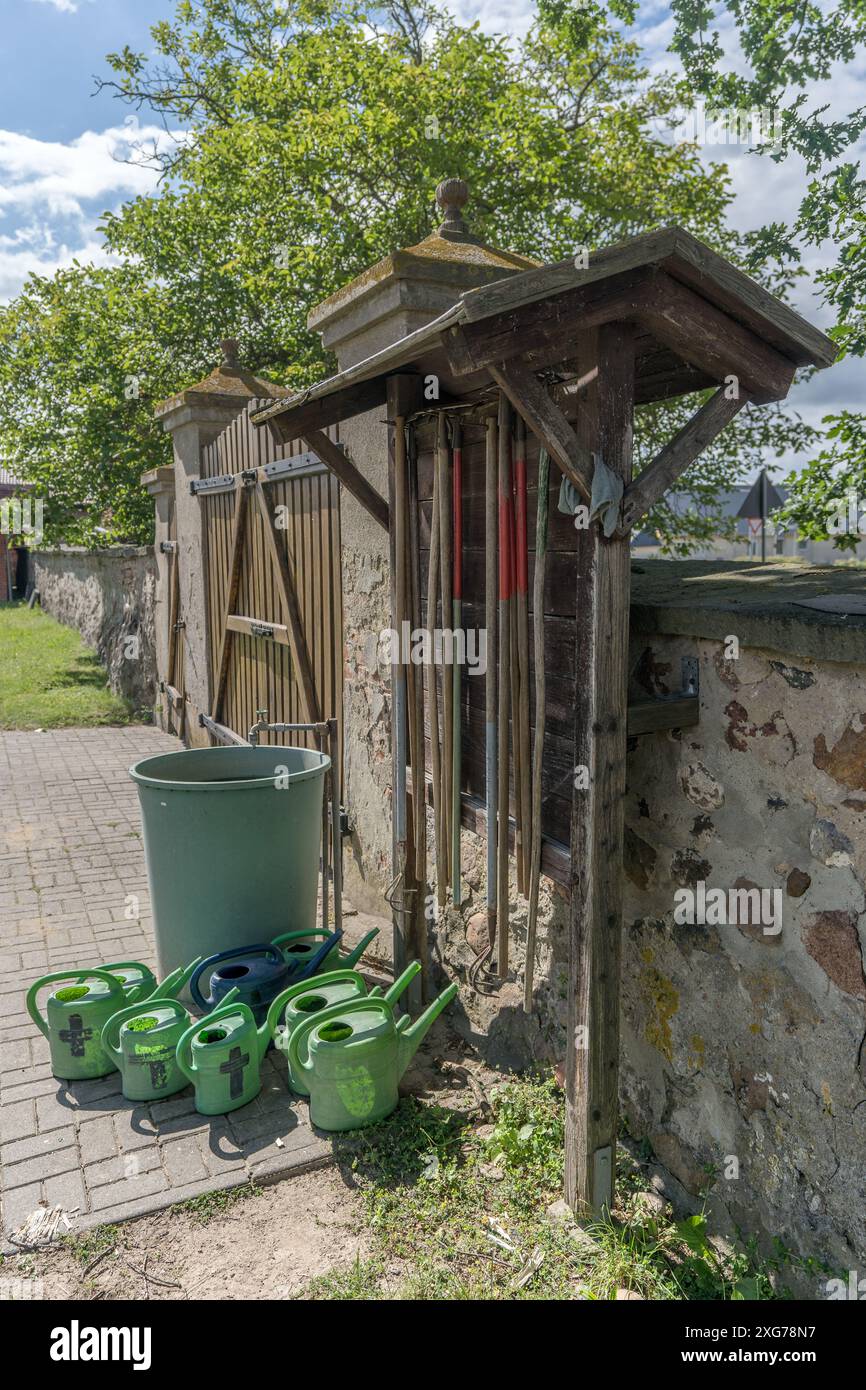 Watering cans and rakes on a cemetery wall Stock Photo