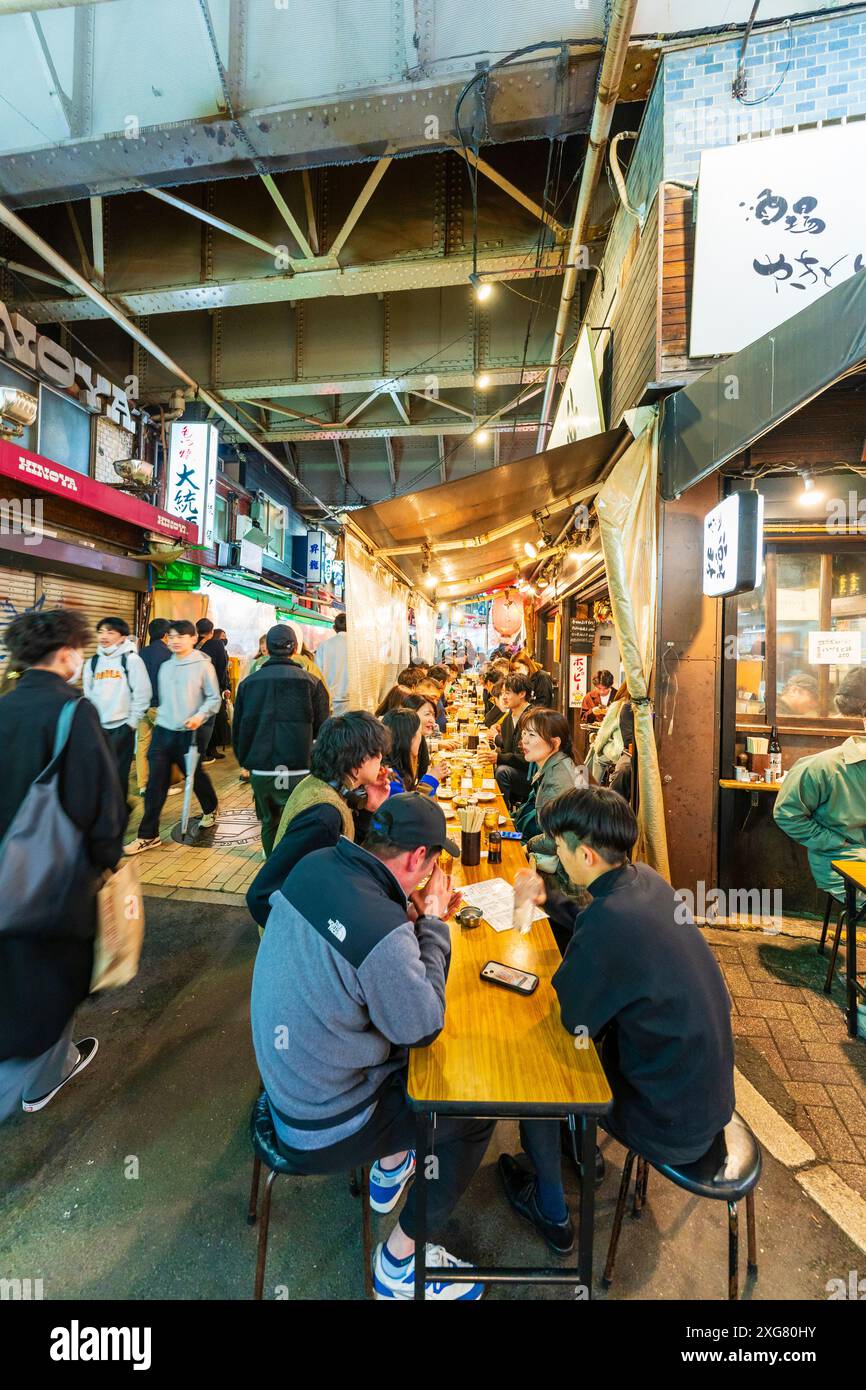 View along table of people sitting dining outside the busy Gyukatsu Motomura Ueno tonkatsu ramen restaurant in the popular Ameyoko Ueno area in Tokyo. Stock Photo