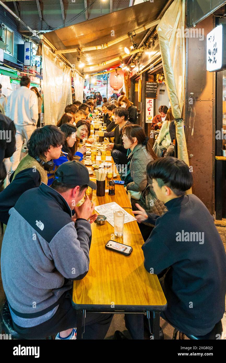 View along table of people sitting dining outside the busy Gyukatsu Motomura Ueno tonkatsu ramen restaurant in the popular Ameyoko Ueno area in Tokyo. Stock Photo