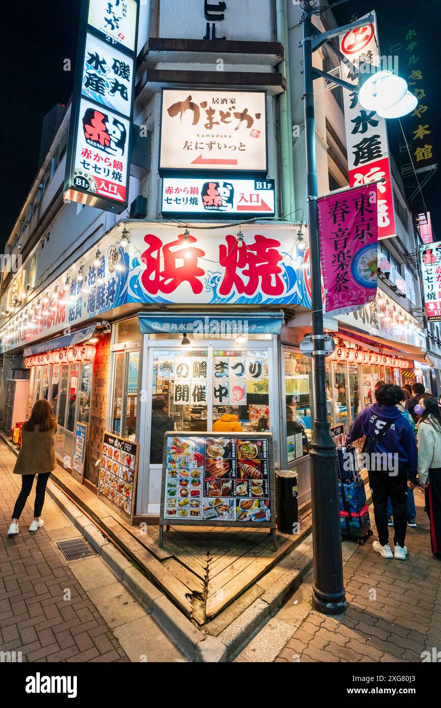 The Isomaru Suisan izakaya restaurant at night with people outside looking at menus boards in the popular district of Ameyoko Ueno in Tokyo. Stock Photo