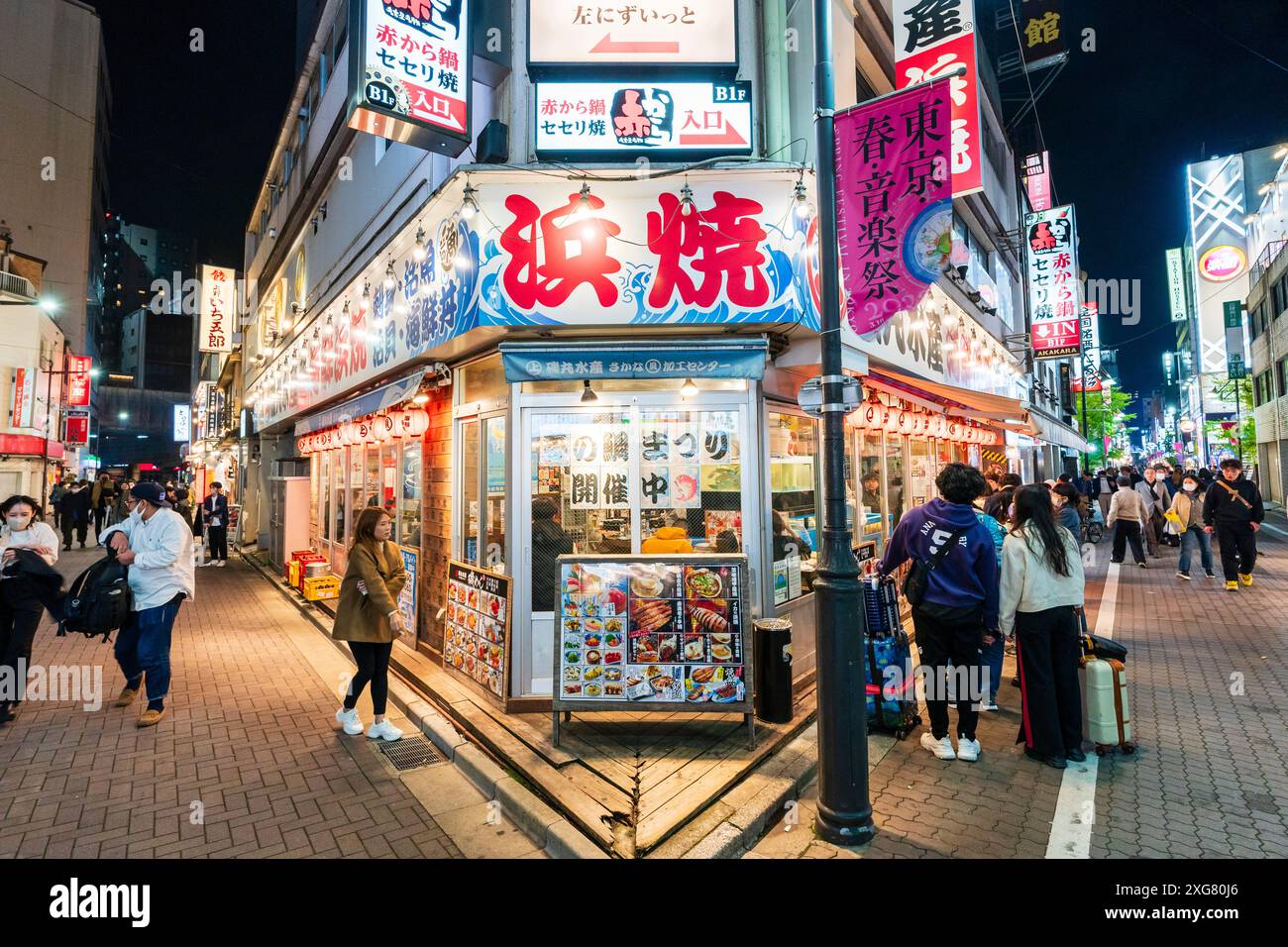 The Isomaru Suisan izakaya restaurant at night with people outside looking at menus boards in the popular district of Ameyoko Ueno in Tokyo. Stock Photo