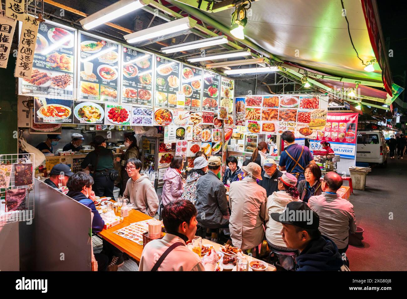 Diners sitting at tables on the pavement outside a Chinese restaurant in the evening in the popular nightlife district Ueno Ameyoko, Tokyo. Stock Photo