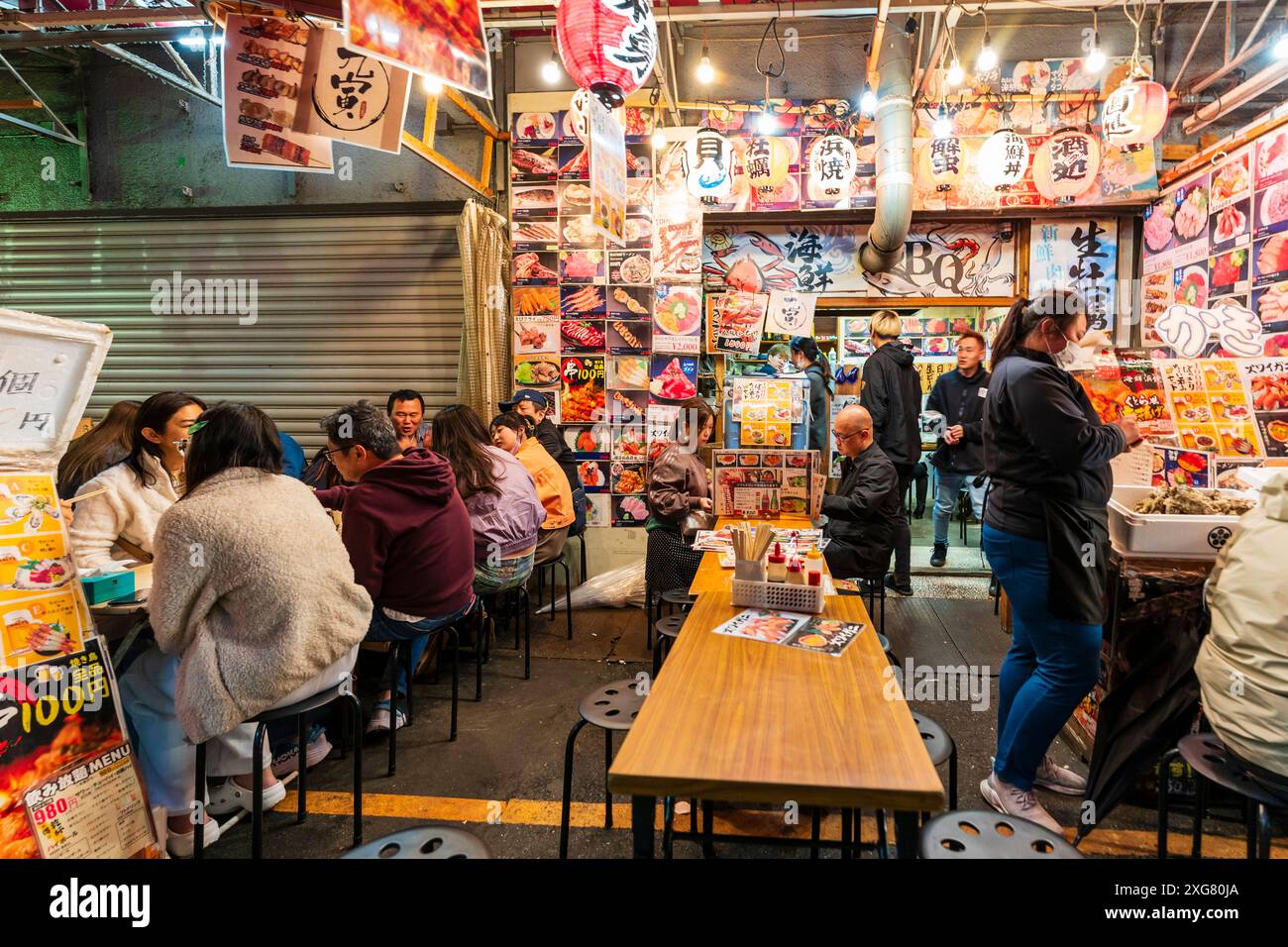 Diners sitting at tables on the pavement outside a Japanese Izakaya restaurant in the evening in the popular nightlife district Ueno Ameyoko, Tokyo. Stock Photo