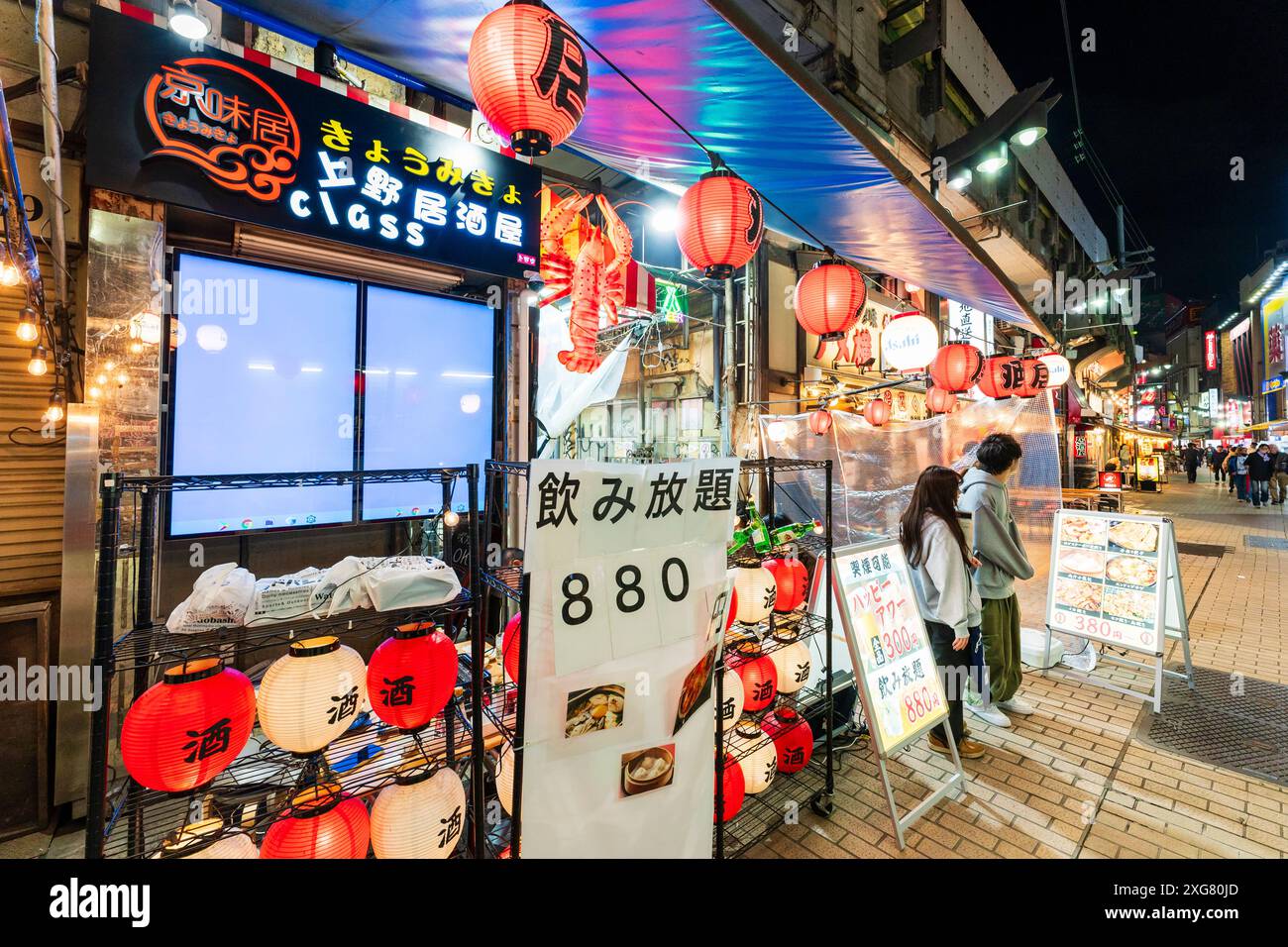 Two greeters standing on the pavement in the entrance of a Japanese izakaya restaurant at nighttime on the Ameyokocho shopping street in Ueno, Tokyo. Stock Photo