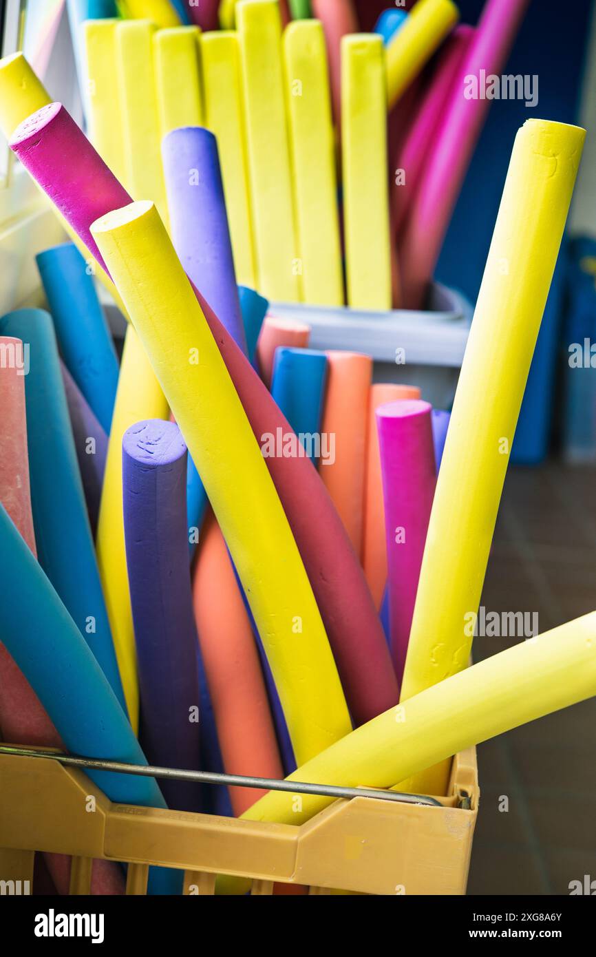 Brightly colored foam pool noodles stored in a container at an indoor swimming pool, ready for aquatic exercises and swimming activities. Stock Photo