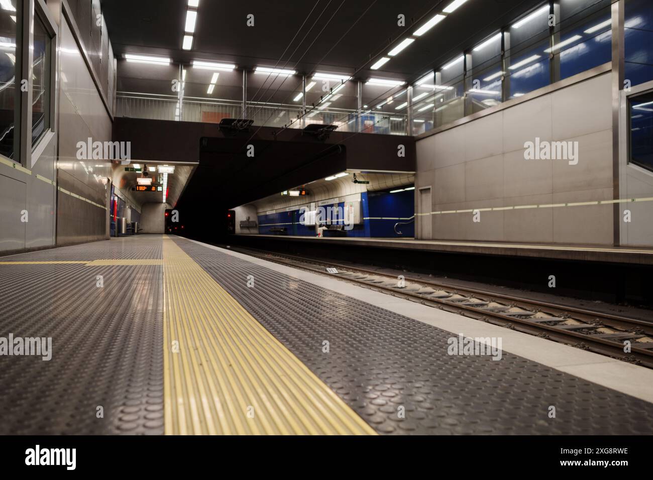 Selective focus and low angle view at underground subway platform with sleek design elements, featuring bright overhead lighting, blue and gray color Stock Photo