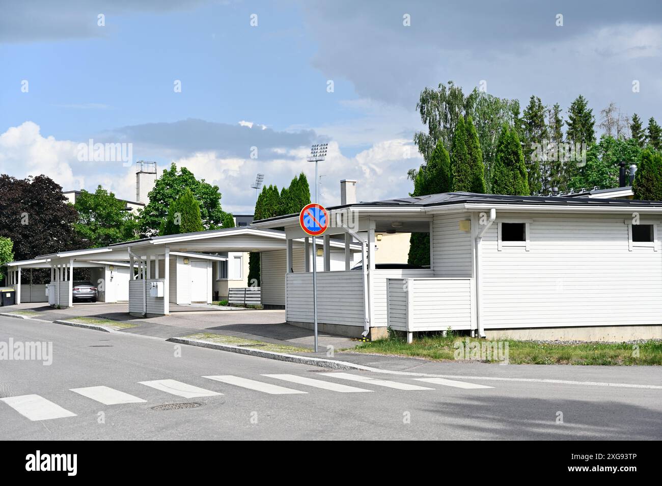 This photo depicts a peaceful suburban neighborhood with modern white houses featuring carports. A crosswalk and a no parking sign are visible on the Stock Photo