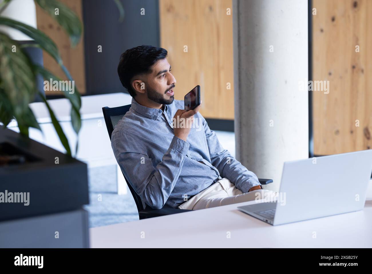 Using smartphone for voice command, man working with laptop in office Stock Photo