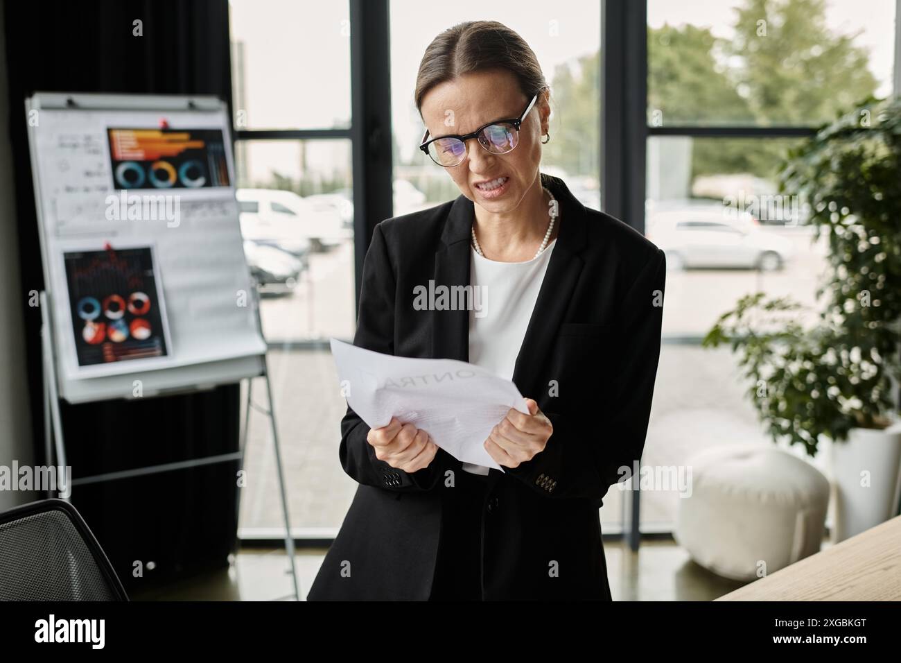 Middle-aged businesswoman experiencing stress and mental exhaustion while reviewing a document in her office. Stock Photo