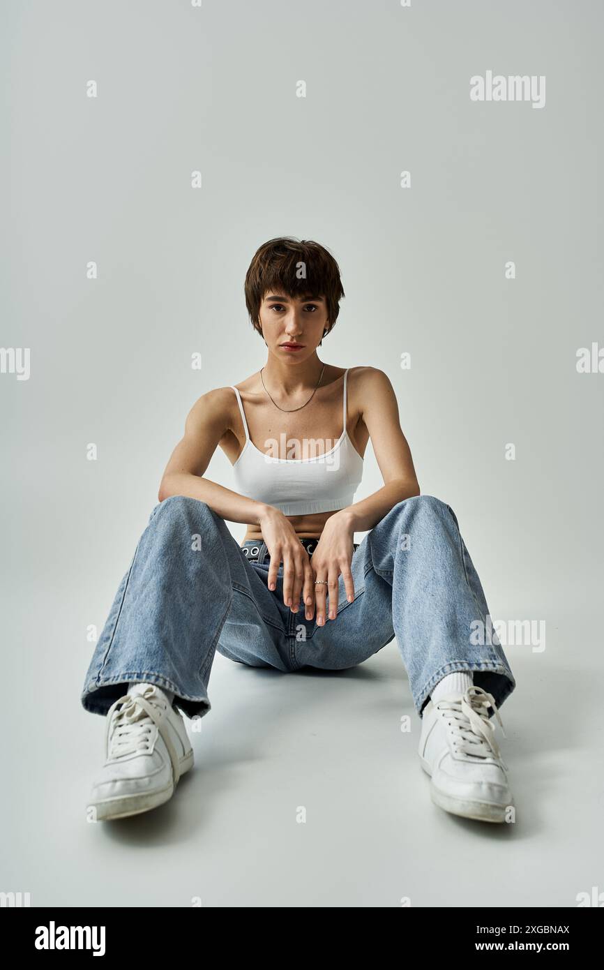 Young woman in white tank top and jeans sitting gracefully on floor ...